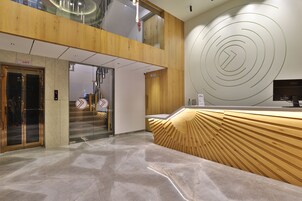 Un área de recepción moderna con un mostrador de madera, piso de mármol y un ascensor de vidrio.