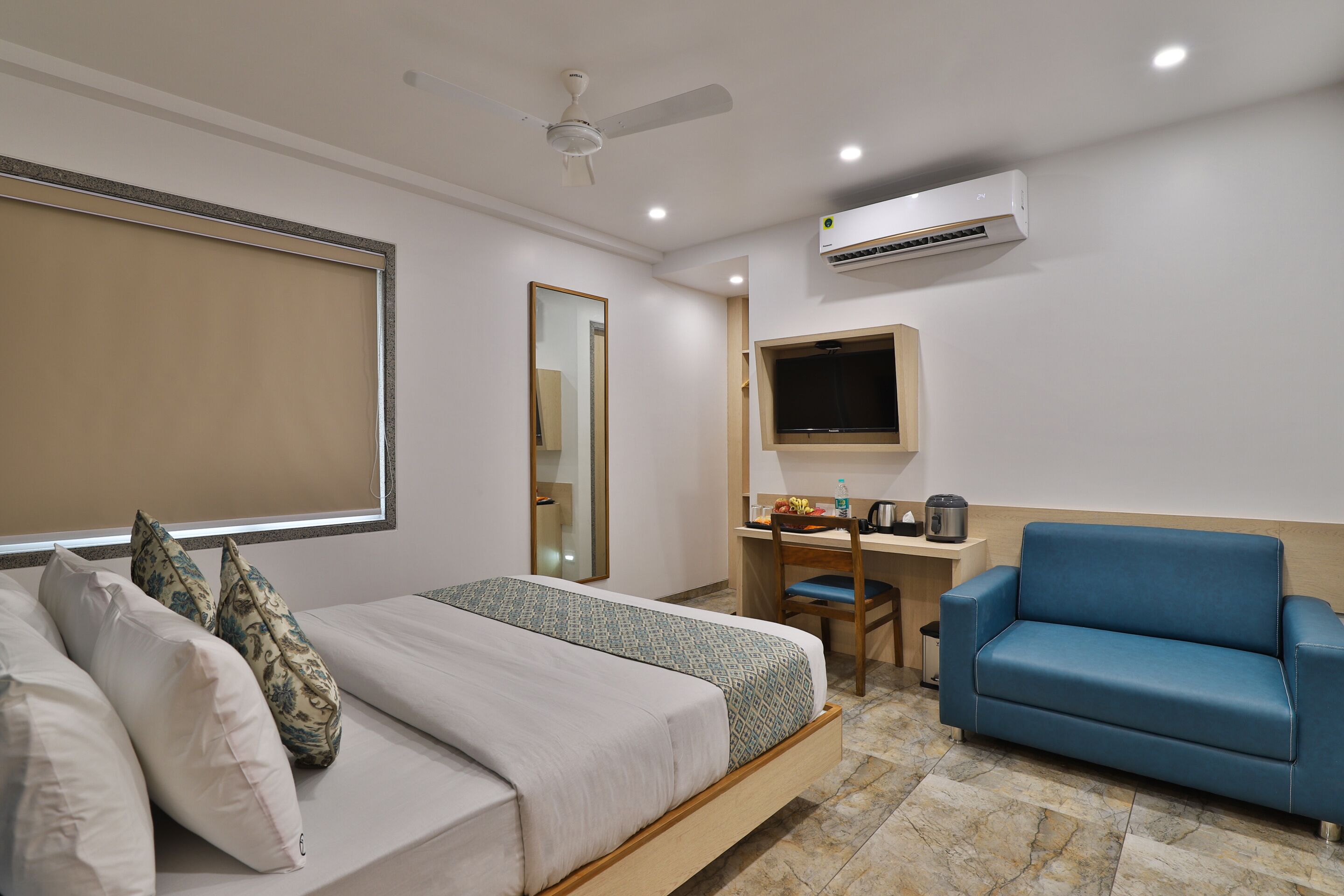 Une chambre d’hôtel avec un lit, un bureau, un canapé bleu, une télévision et un appareil de climatisation.