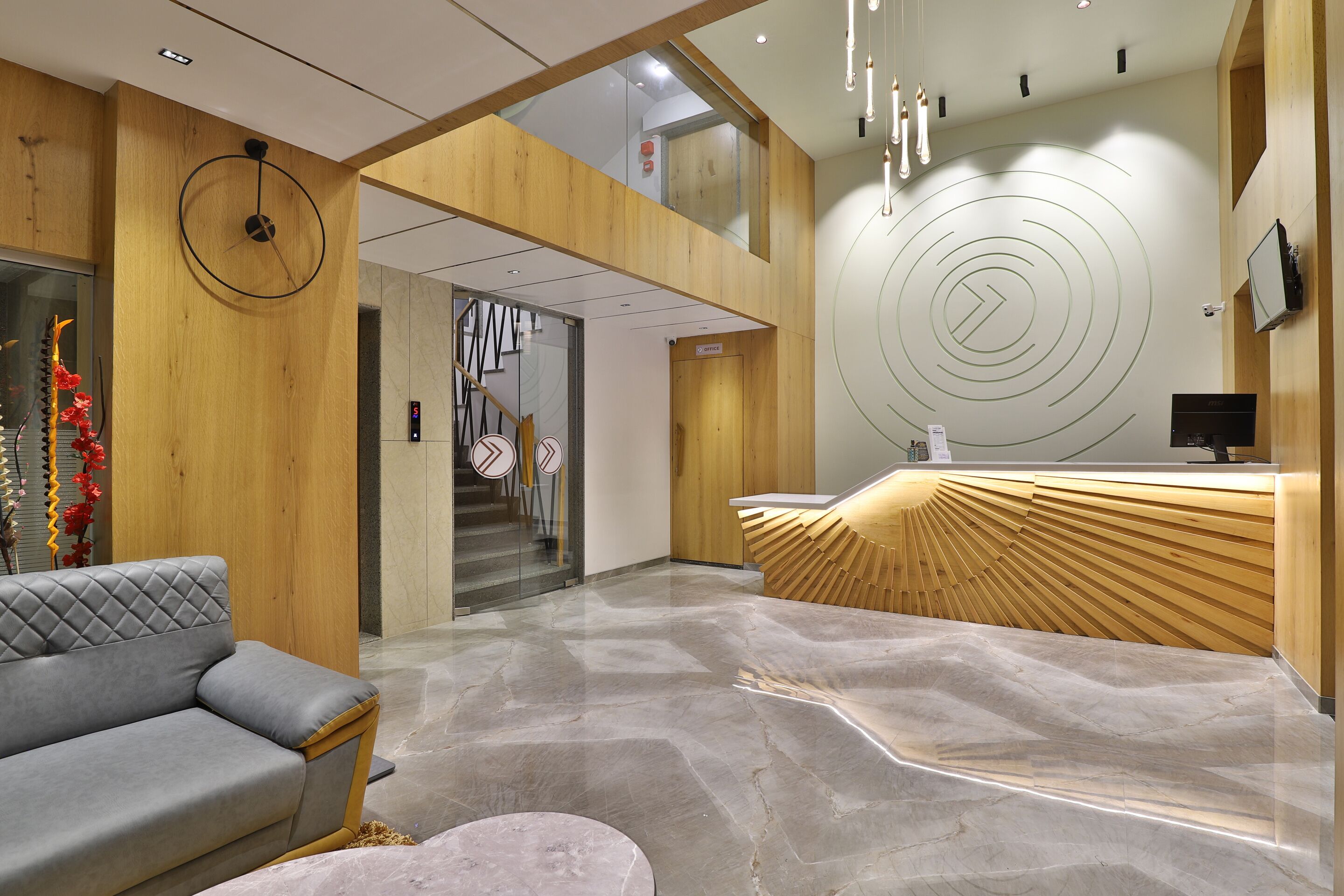Un espace d’accueil moderne avec un comptoir de réception en bois, un canapé gris et un sol en marbre.