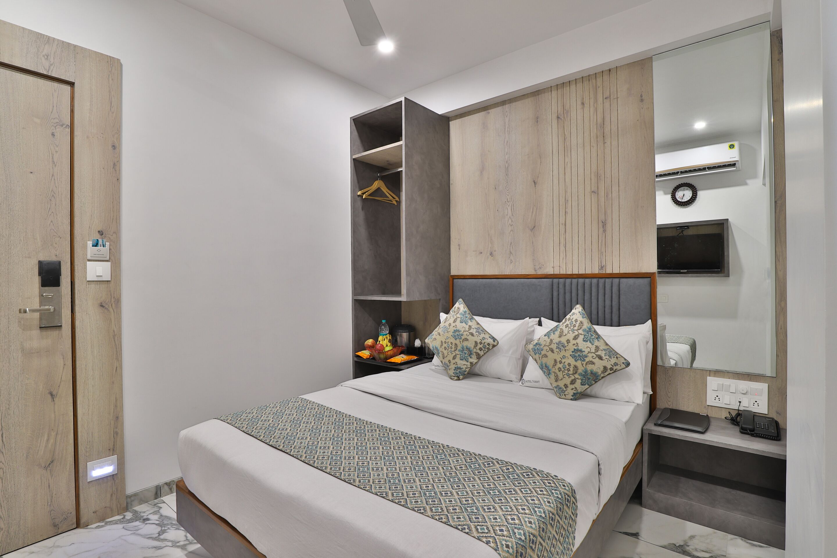 Une chambre d’hôtel moderne équipée d’un lit, d’une armoire, d’une table de chevet avec une lampe et d’un téléviseur fixé au mur.