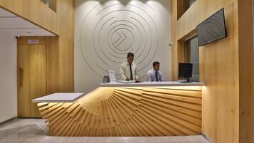 A reception desk with a unique wooden design, two staff members, and a modern wall with circular patterns.