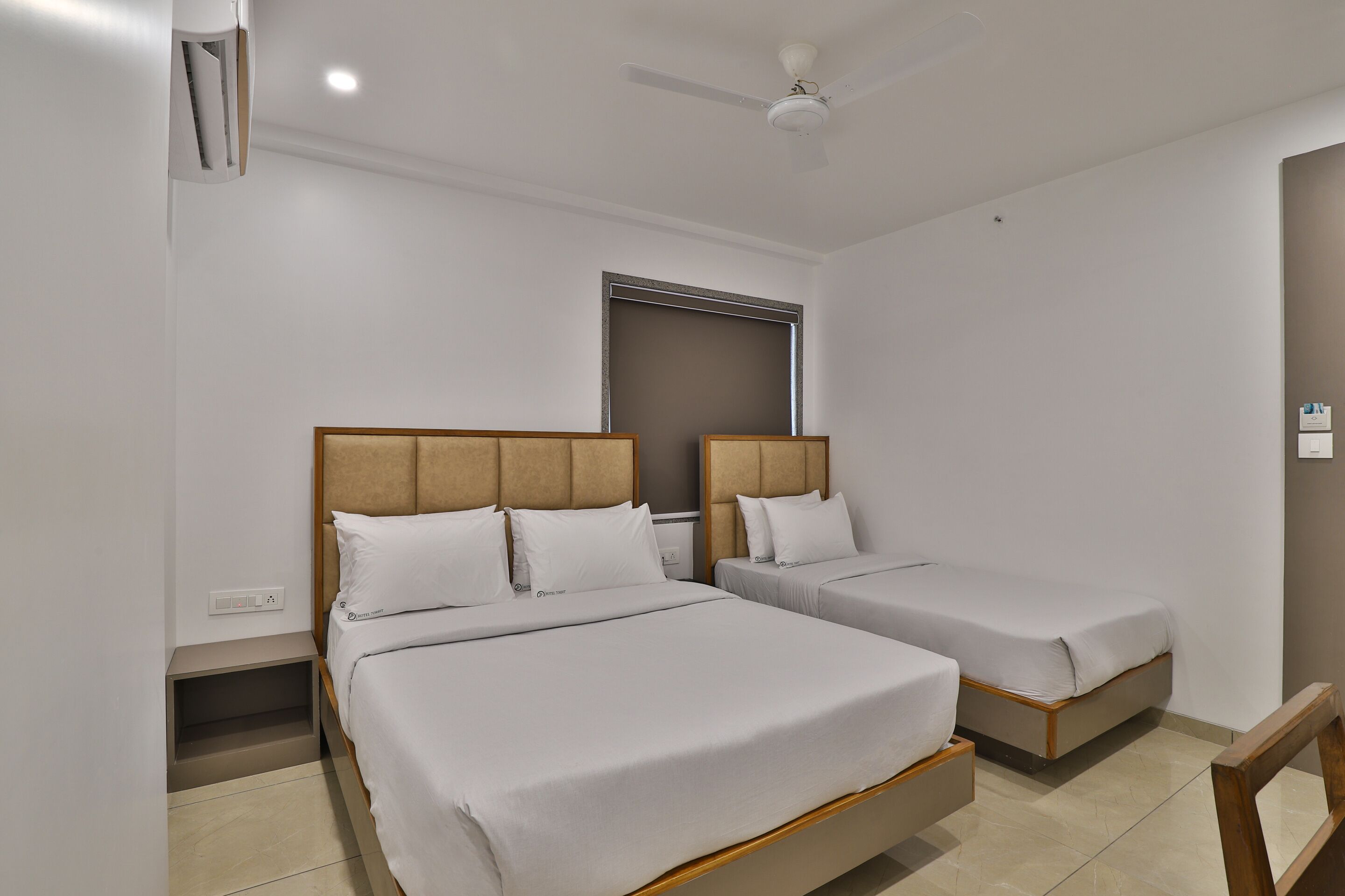 A hotel room with two single beds, a ceiling fan, a window, and a small bedside table.
