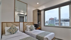 Quarto de hotel com duas camas, uma janela grande, um espelho e um guarda-roupa embutido.