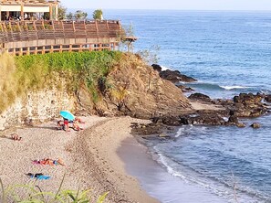 Un hôtel situé sur la côte, avec vue sur la plage, un rivage rocheux et une architecture caractérisée par un toit en pente donnant sur la mer.