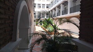 A covered walkway with brick walls and white columns, leading to a courtyard with palm trees and a white building in the background. - Benalmar Playa (Benalmádena)