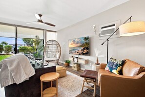 A modern living room with a sofa, a chair, a small table, a floor lamp, a television, and a large window.