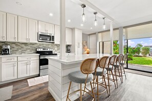 Une cuisine moderne avec des meubles blancs, des appareils en acier inoxydable et un coin bar équipé de tabourets.