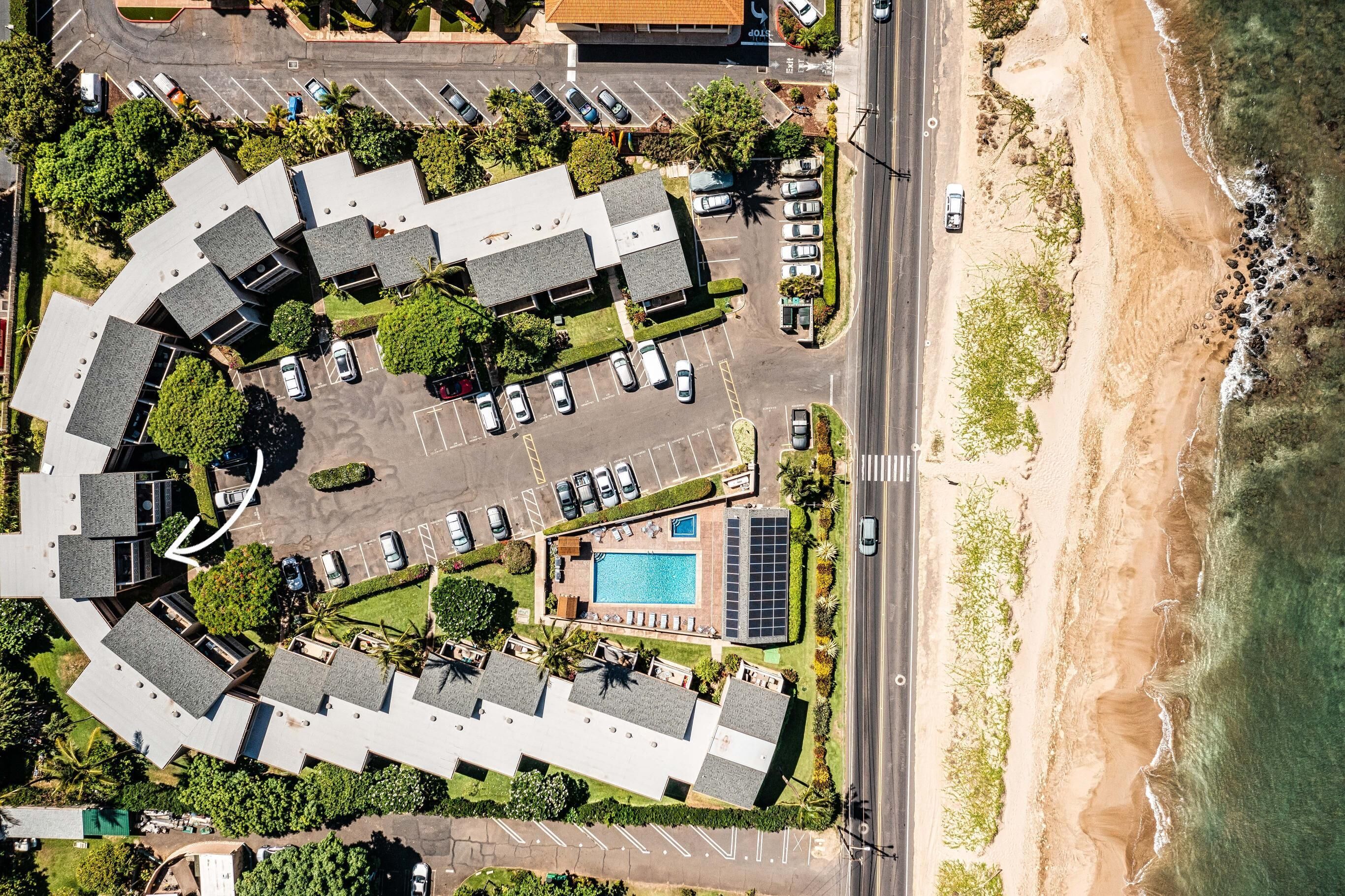 An aerial view of a hotel with a swimming pool, parking lot, and beachfront access.