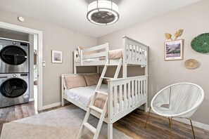 A bunk bed with a ladder, a washing machine, a white chair, and wall decorations in a room with wooden flooring.