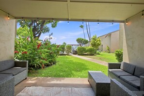 A covered patio with wicker furniture and a view of a well-maintained lawn and trees.