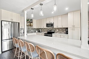 A modern kitchen with white cabinetry, stainless steel appliances, a large island with bar seating, and pendant lighting.