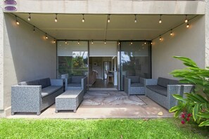 Un espace extérieur aménagé avec des meubles en osier, une entrée avec une porte vitrée et un patio couvert.