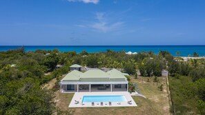 A modern house with a swimming pool, surrounded by lush greenery and a view of the ocean.