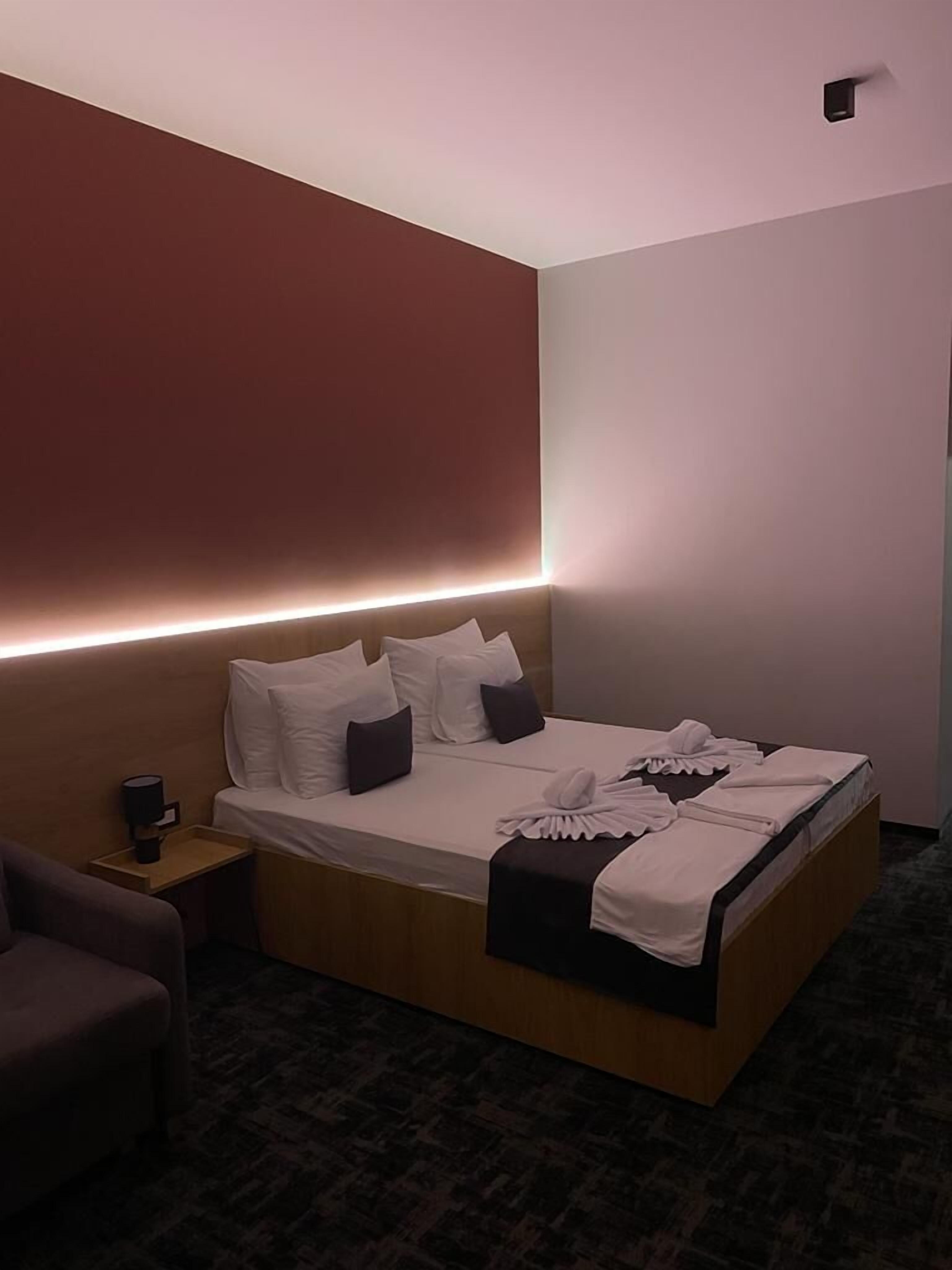 Une chambre d’hôtel moderne avec un grand lit, une table de chevet avec une lampe et un petit fauteuil.