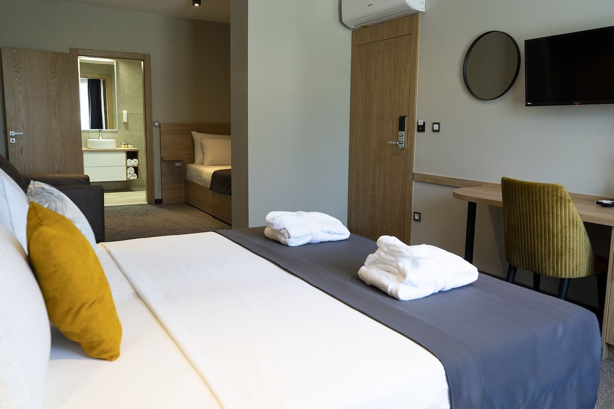 Ein Hotelzimmer mit einem großen Bett, einem Schreibtisch, einem Sessel, einem Fernseher und einem durchgegangenen Tür erkennbaren Badezimmer.