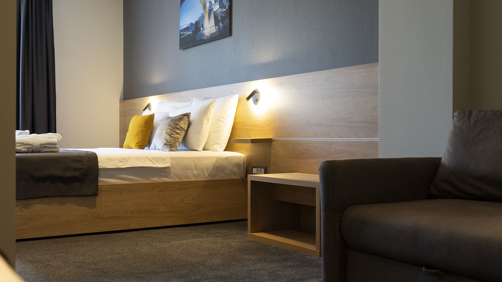 Et hotelværelse med en seng, et natbord, en stol og et billede hængende på væggen.