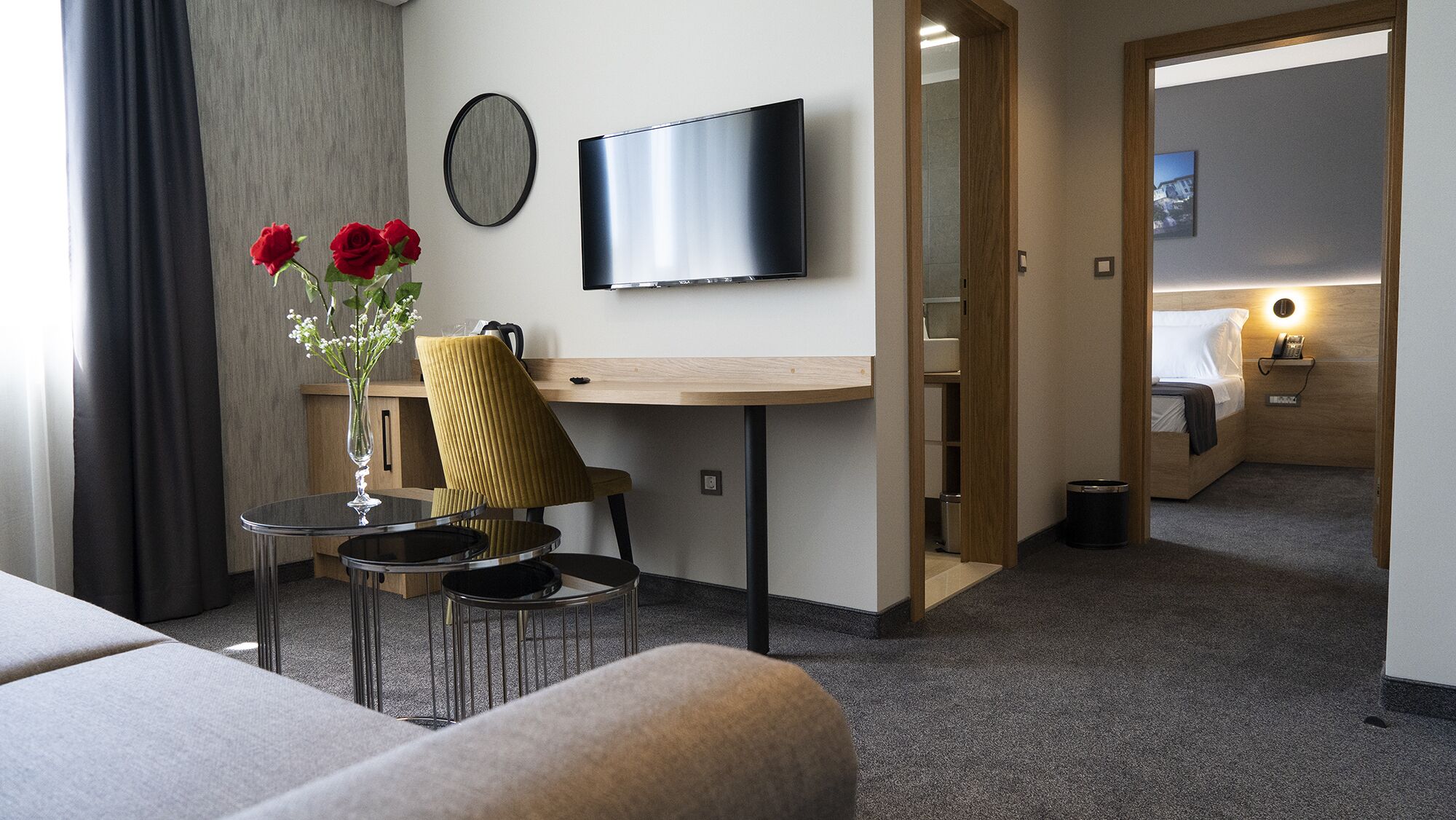 Una camera d'albergo con un letto, una scrivania con una sedia, una TV e un vaso con fiori.