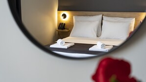 Une chambre d’hôtel avec un lit, deux oreillers, une table de chevet avec une lampe et un miroir qui reflète la pièce.