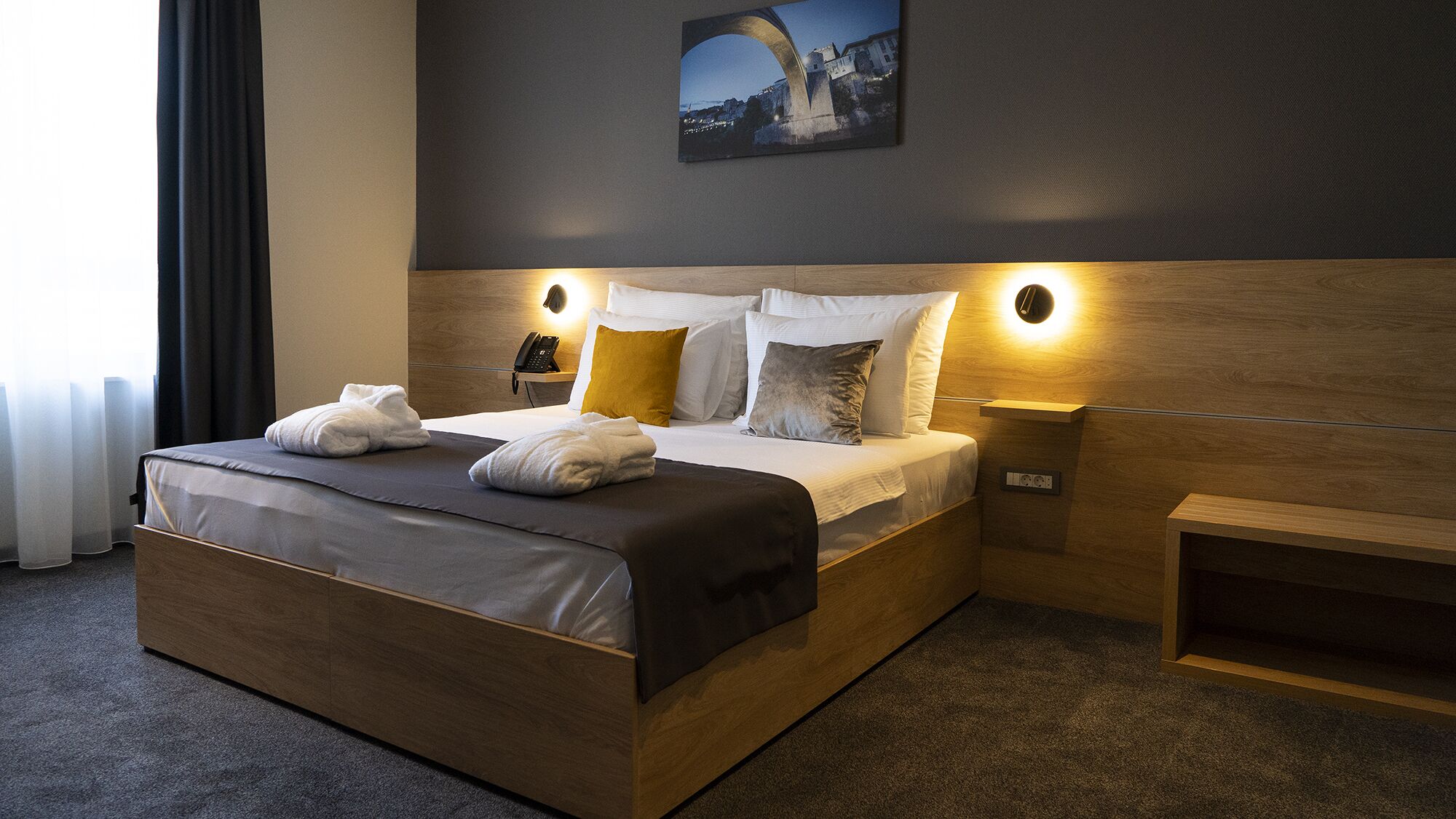 A hotel room with a large bed, two bedside tables, a nightstand, and a painting on the wall.