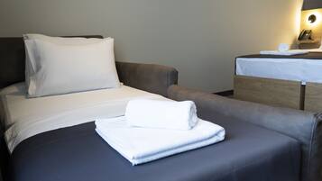 A hotel room with a bed, a bedside table with a lamp, and a folded towel on the bed.