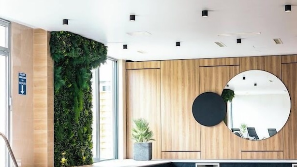 Un espace piscine intérieur moderne, avec un mur en bois, un jardin vertical et un grand miroir rond.