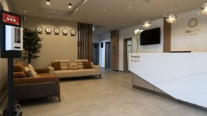 Un espace d’accueil d’hôtel comprenant un comptoir de réception, un canapé et une horloge indiquant plusieurs fuseaux horaires.