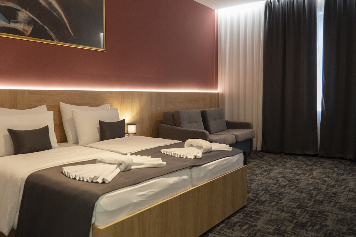 Ein Hotelzimmer mit einem großen Bett, einer Sitzecke, einem Schreibtisch und einem Fenster mit Vorhängen.
