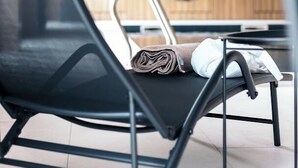 Un espace d’attente moderne avec un fauteuil noir, un mur en bois et un grand miroir rond qui reflète la pièce.