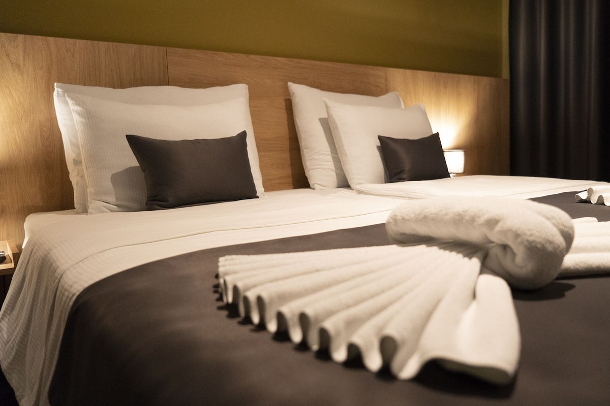 Ein Hotelzimmer mit einem großen Bett, vielen Kissen und ordentlich drapierten Handtüchern.