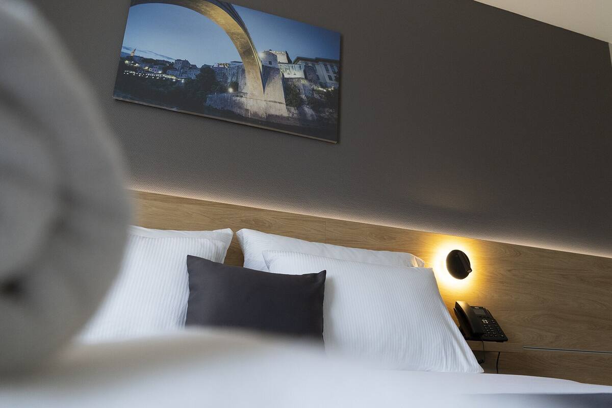 Ein Hotelzimmer mit einem Bett, weißen Kissen, einem dunklen Kissen, einem Nachttisch mit Telefon und einer Wandleuchte.