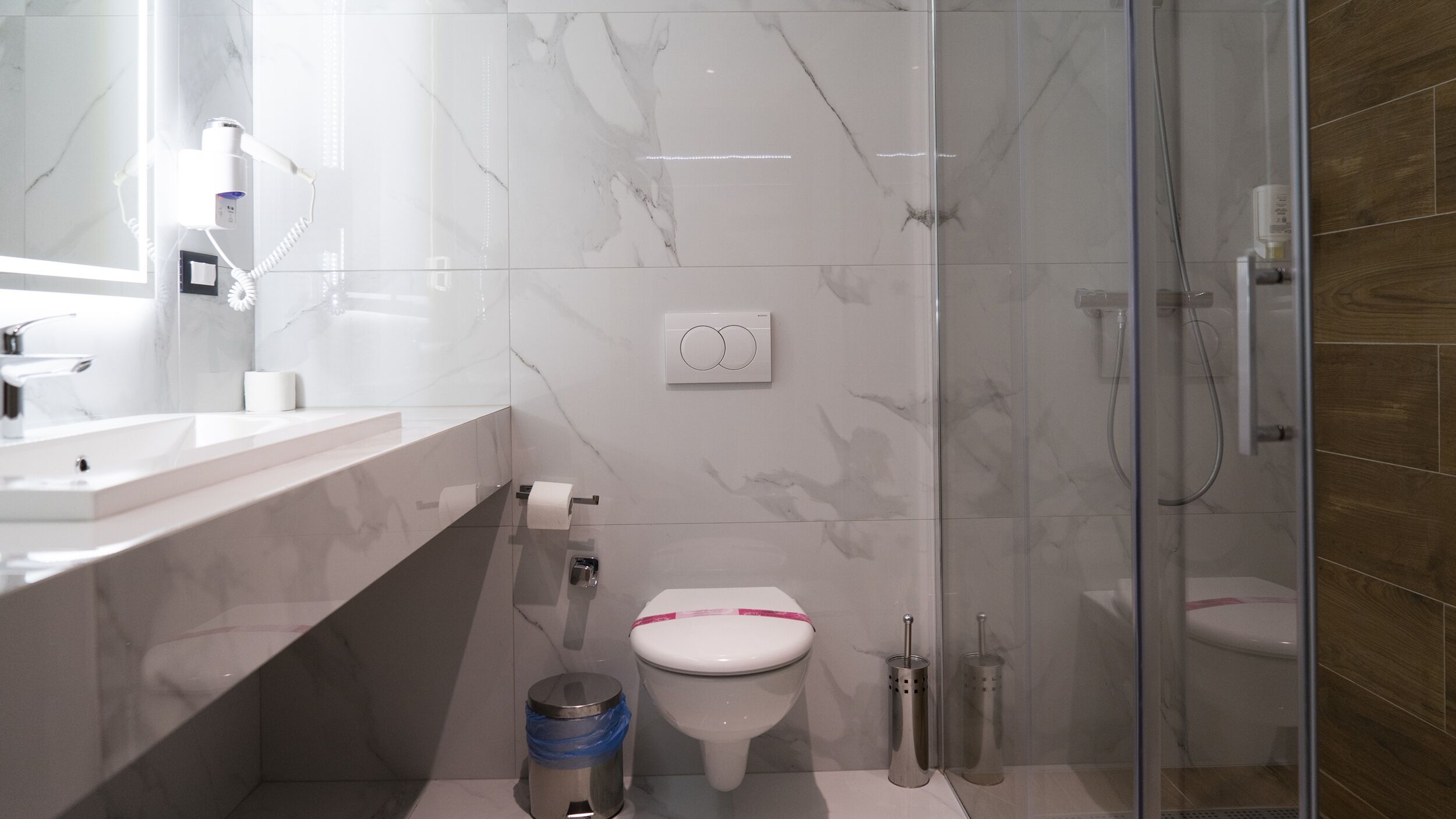 Un baño moderno con un lavabo de mármol blanco, inodoro y cabina de ducha de vidrio.