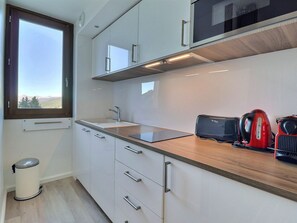 Una cocina moderna con armarios blancos, encimera de madera, una ventana y un cubo de basura.