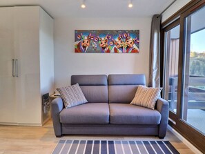 Una sala de estar moderna con un sofá gris, almohadas a rayas, un cuadro abstracto colorido y un amplio ventanal con vistas.