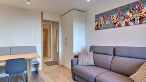 A modern living room with a sofa, a dining table, and a chair. There is a colorful abstract painting on the wall.