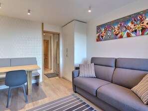 A modern living room with a sofa, a dining table, and a chair. There is a colorful abstract painting on the wall.