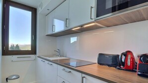 A modern kitchen with white cabinets, a wooden countertop, a window, and a trash can.
