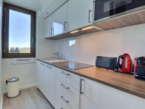 A modern kitchen with white cabinets, a wooden countertop, a window, and a trash can.