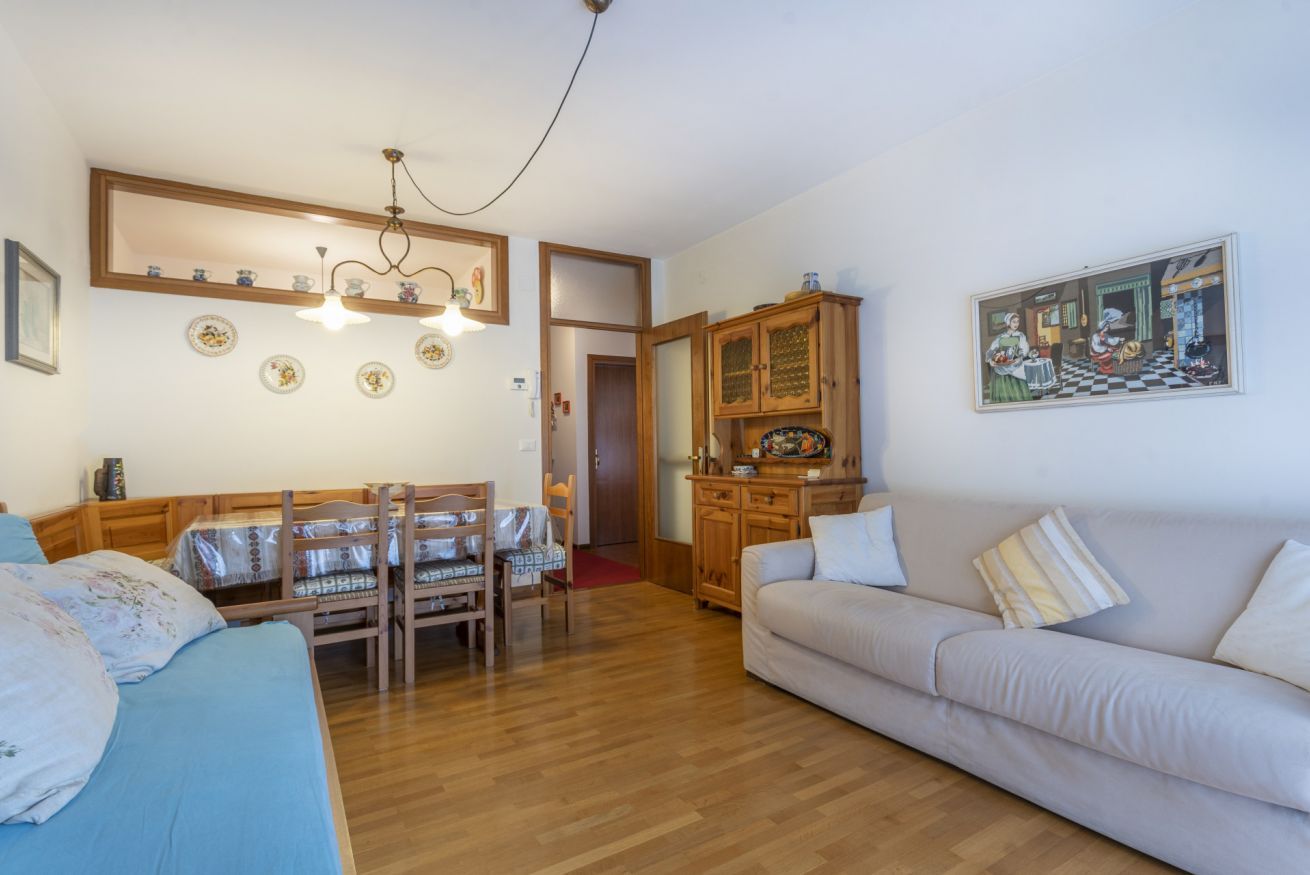 Un soggiorno con un divano, un tavolo da pranzo con sedie, un mobile in legno e un quadro appeso al muro.