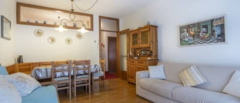 A living room with a sofa, a dining table with chairs, a wooden cabinet, and a painting on the wall.