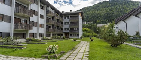 A multi-story building with balconies, a paved courtyard, and a mountainous backdrop.