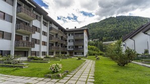 A multi-story building with balconies, a paved courtyard, and a mountainous backdrop.