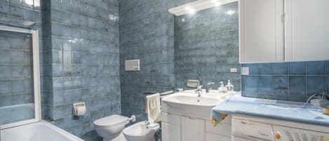 A bathroom with a bathtub, toilet, bidet, sink, and washing machine.
