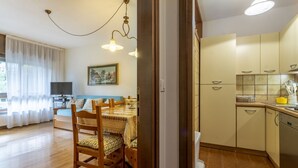 A room with a dining table, chairs, a television, a bed, and a kitchen area with cabinets and a sink.