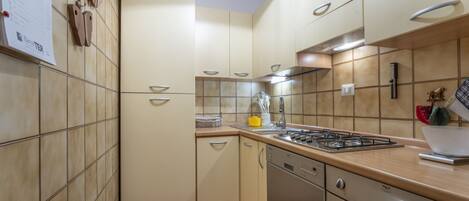 A kitchen with beige cabinets, a gas stove, a dishwasher, and a tiled backsplash.