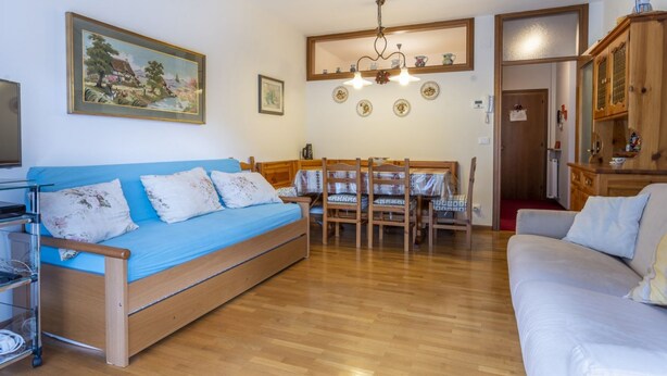 A cozy living room with a blue sofa, wooden dining table, and a wooden cabinet. - GuestHost - Typical vintage flat with terrace (overlooking the Julian Alps!) That can accommodate up to 4 people, located in a quiet area with common garden a stone's throw from the center of Tarvisio. Thanks to its strategic position, from the apartment (Tarvisio)