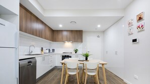 A modern kitchen with white cabinetry, wooden flooring, and a dining area with a table and chairs. - Wentworthville 2 Bedrooms 2 Bathrooms with Free Parking by KozyGuru (Wentworthville)
