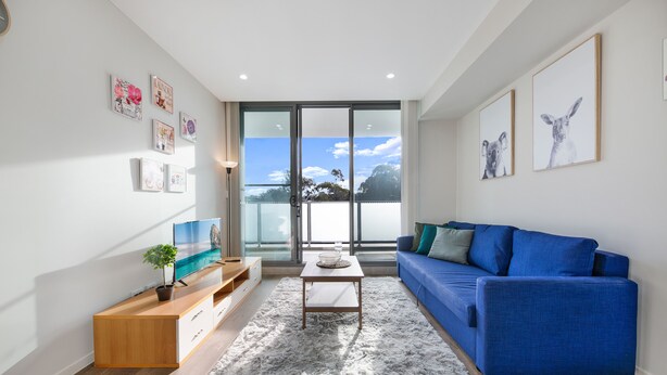 A modern living room with a blue sofa, a wooden coffee table, and a grey rug. - Wentworthville 2 Bedrooms 2 Bathrooms with Free Parking by KozyGuru (Wentworthville)