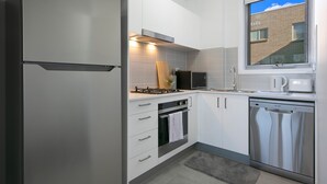 Eine moderne Küche mit weißen Schränken, Edelstahlgeräten, einem Fenster mit Blick auf ein Ziegelgebäude und einem grauen Teppichboden.