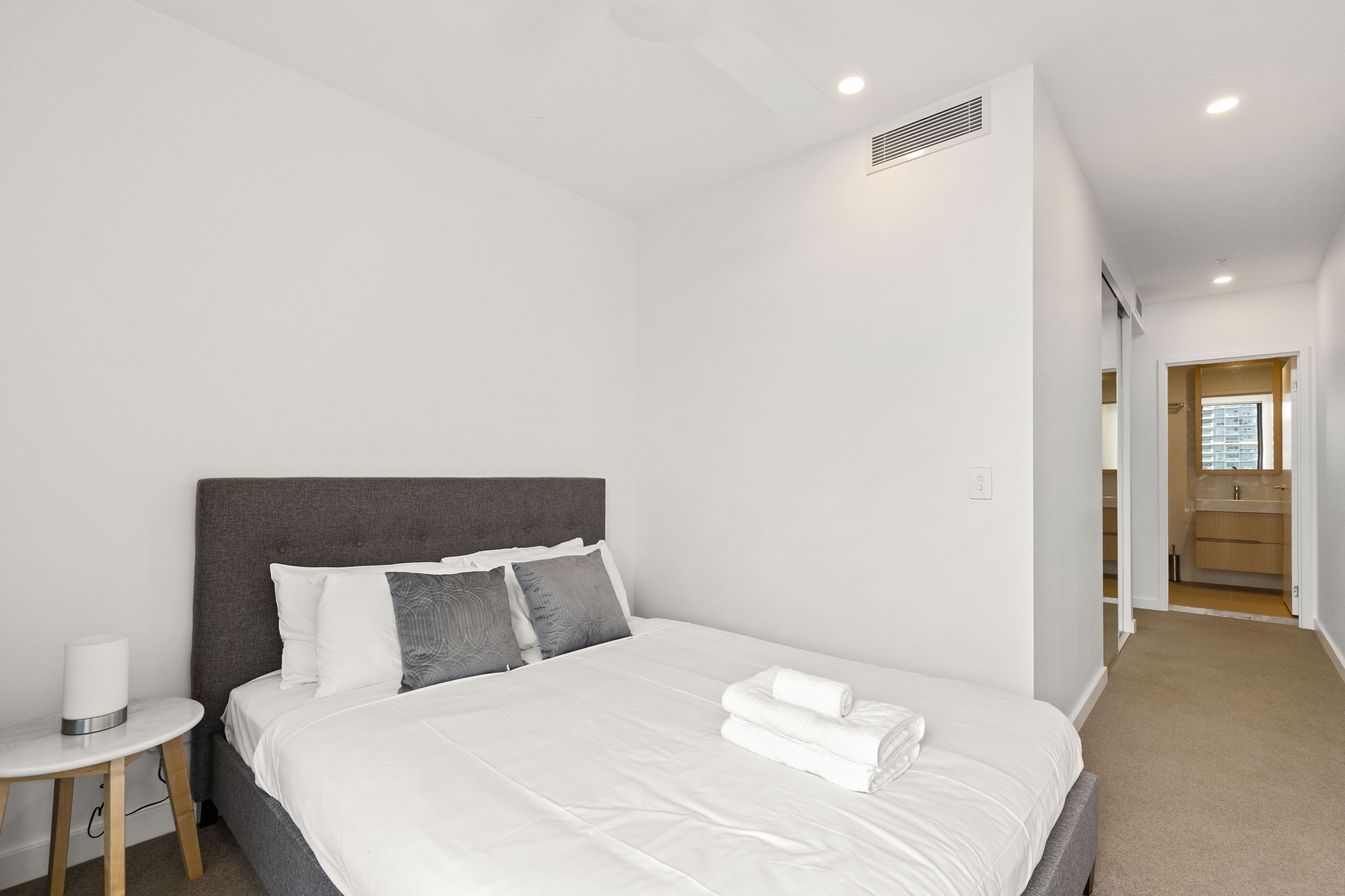 Habitación de hotel moderna con una cama grande, una mesita de noche y vistas al baño.