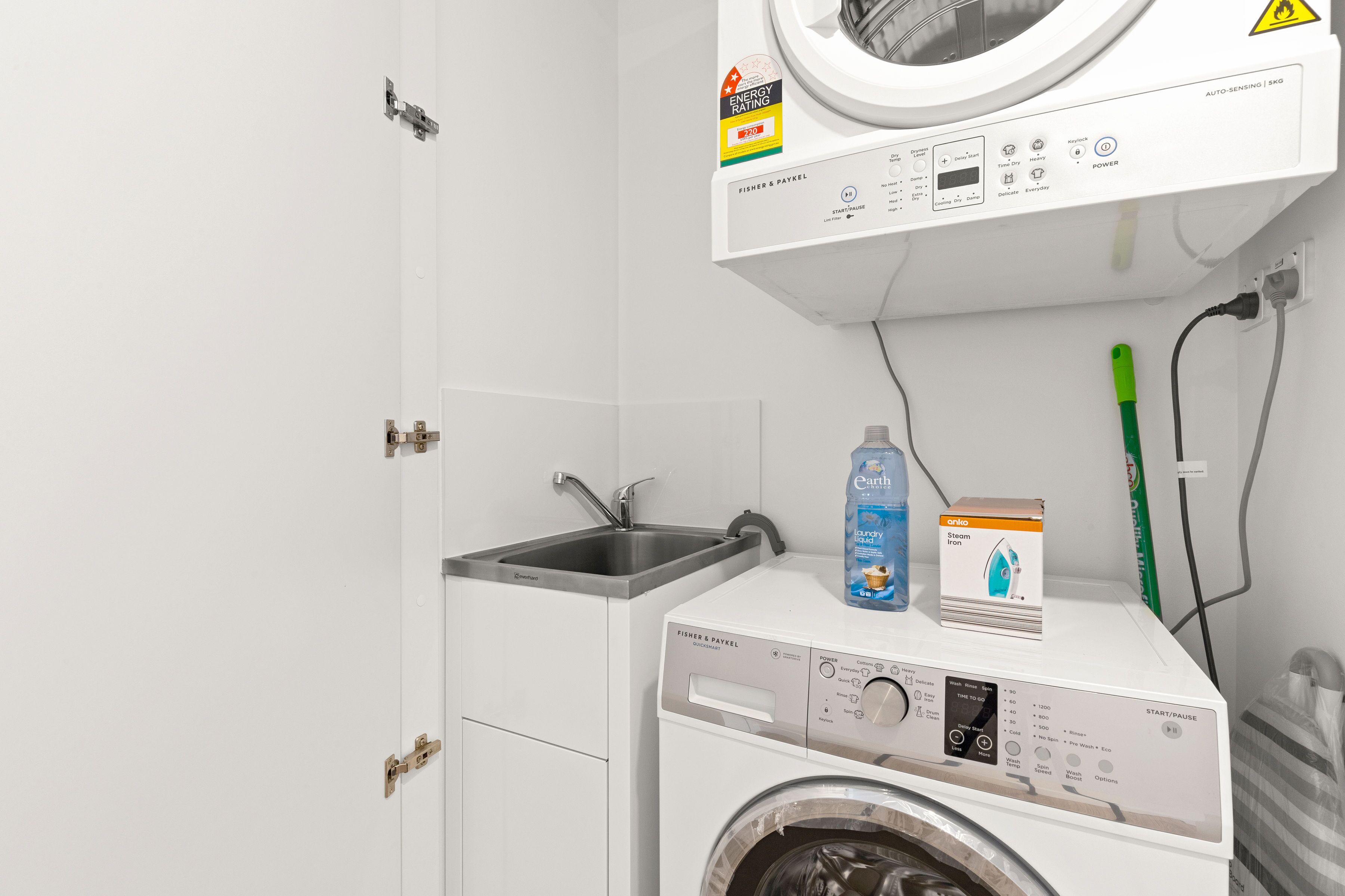 A compact laundry area with a washing machine, a sink, and a bottle of laundry liquid.
